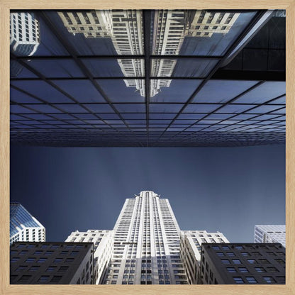 A framed, low-angle photograph capturing a stark white skyscraper against a deep blue sky, with its perfect reflection mirrored in the dark glass facade of an overhanging building, creating a surreal and symmetrical composition. Wall Art