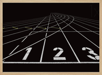 A framed, high-contrast graphic of a black running track from a low-angle perspective at the starting line. White lines delineate the lanes, with the numbers 1, 2, and 3 stenciled in the foreground. The track curves and recedes into the distance, creating a strong sense of perspective. Decor
