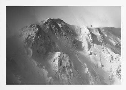 A dramatic black and white photograph of a person standing alone on the ridge of a massive, snow-covered mountain, emphasizing the scale and solitude of the vast, rugged landscape, all presented in a silver frame. Wall Art
