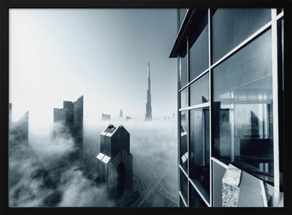 A framed black and white photograph with a cool blue tint, depicting the Dubai skyline from a high-rise window, with skyscrapers including the Burj Khalifa piercing through a thick blanket of fog. Artwork