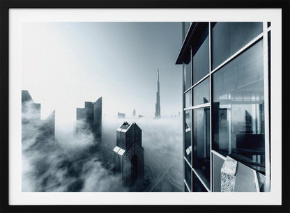 A framed black and white photograph with a cool blue tint, depicting the Dubai skyline from a high-rise window, with skyscrapers including the Burj Khalifa piercing through a thick blanket of fog. Artwork