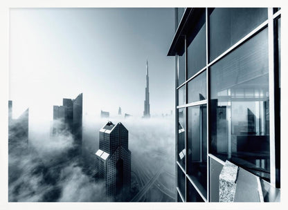 A framed black and white photograph with a cool blue tint, depicting the Dubai skyline from a high-rise window, with skyscrapers including the Burj Khalifa piercing through a thick blanket of fog. Artwork