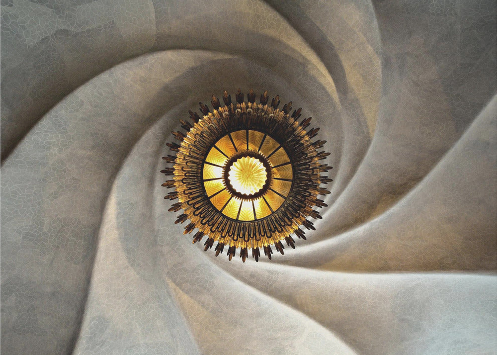 A low-angle, centered photograph looking up at an ornate, golden sunburst chandelier hanging from the vortex of a swirling, textured cream-colored ceiling, enclosed in a silver frame. Poster