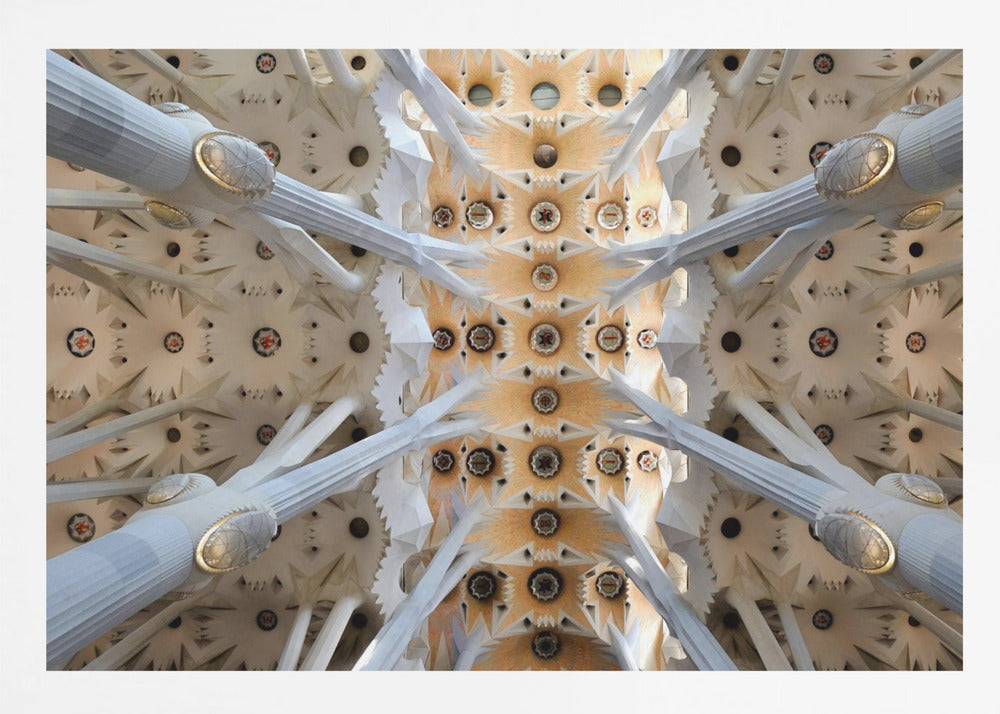 A symmetrical photograph looking directly up at the ornate, geometric ceiling of the Sagrada Familia. White, tree-like columns branch out to support the intricate vaulted ceiling, which is detailed with warm orange and gold starburst patterns. Decor