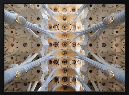 A symmetrical photograph looking directly up at the ornate, geometric ceiling of the Sagrada Familia. White, tree-like columns branch out to support the intricate vaulted ceiling, which is detailed with warm orange and gold starburst patterns. Decor