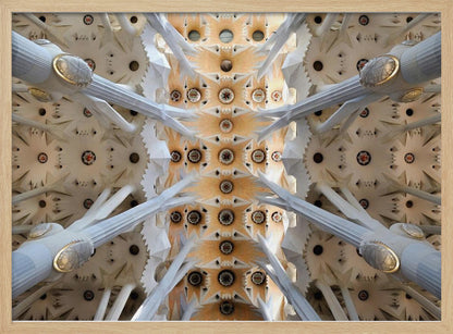 A symmetrical photograph looking directly up at the ornate, geometric ceiling of the Sagrada Familia. White, tree-like columns branch out to support the intricate vaulted ceiling, which is detailed with warm orange and gold starburst patterns. Decor