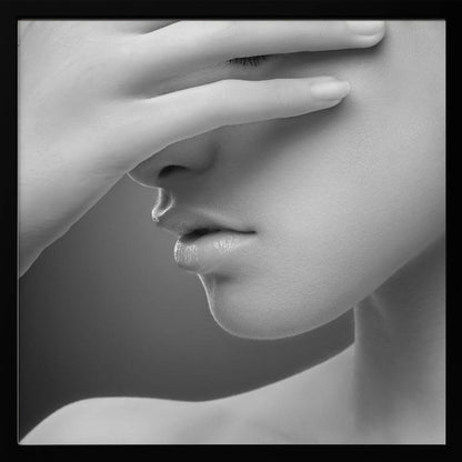 A close-up, black and white photograph of a woman's face. Her hand covers her eyes, revealing only the lower half of her face including her nose, lips, and chin. The image has a soft, sensual quality and is set within a light-colored wooden frame. Decor