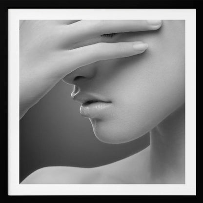 A close-up, black and white photograph of a woman's face. Her hand covers her eyes, revealing only the lower half of her face including her nose, lips, and chin. The image has a soft, sensual quality and is set within a light-colored wooden frame. Decor