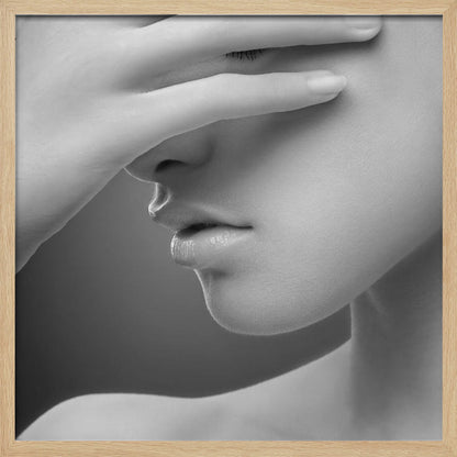 A close-up, black and white photograph of a woman's face. Her hand covers her eyes, revealing only the lower half of her face including her nose, lips, and chin. The image has a soft, sensual quality and is set within a light-colored wooden frame. Decor