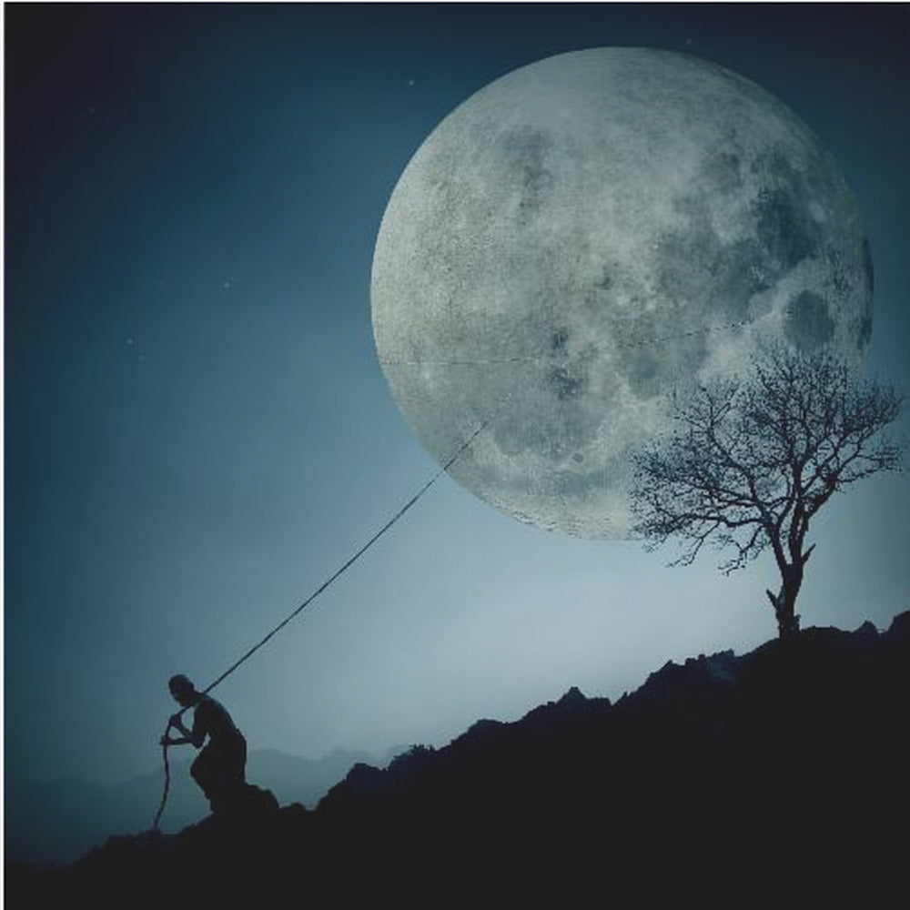 A surreal, framed artwork depicting a silhouette of a person on a dark, rocky hill at night, pulling a rope attached to a massive, detailed full moon, seemingly trying to pull it from the dark blue, star-dusted sky. A bare, silhouetted tree stands on the same hill. Artwork