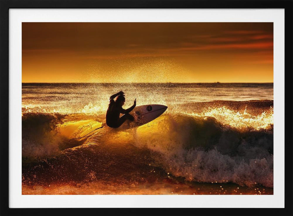 A silhouetted surfer carves a turn on a sun-kissed wave during a vibrant orange sunset, with golden light reflecting off the water and sea spray. Wall Art