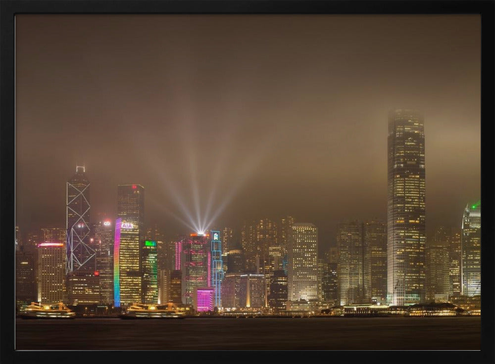A framed photograph of the Hong Kong skyline at night, viewed from across the water. The skyscrapers are brilliantly lit with yellow, white, and colorful lights, and beams of light shoot up into the foggy, glowing sky. Decor