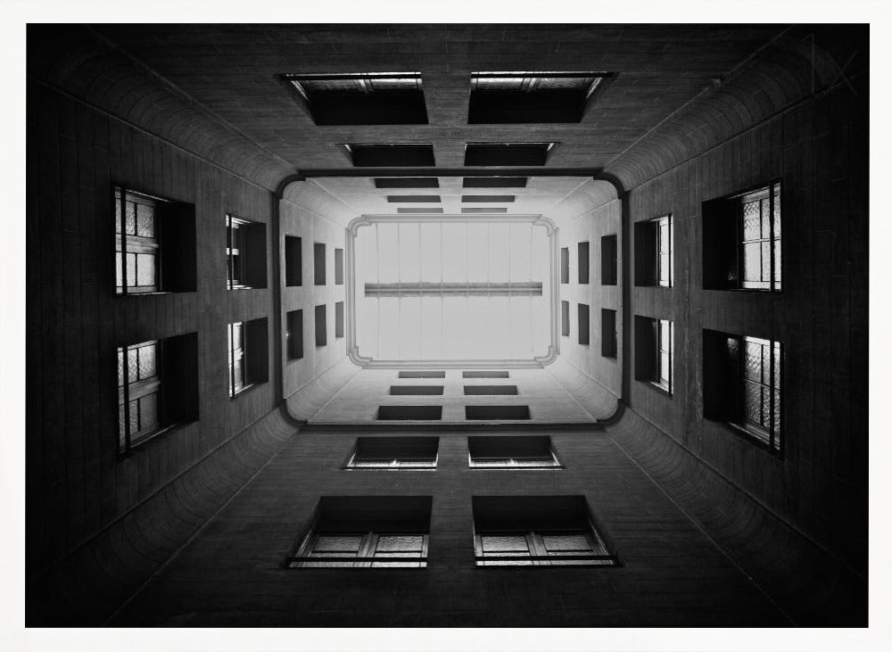 A symmetrical, black and white photograph looking directly up from the base of a building's interior courtyard. The dark walls rise up, lined with rows of windows, creating a powerful sense of perspective that draws the eye to the bright rectangle of the sky or a skylight at the top. The image is enclosed in a simple silver frame. Poster