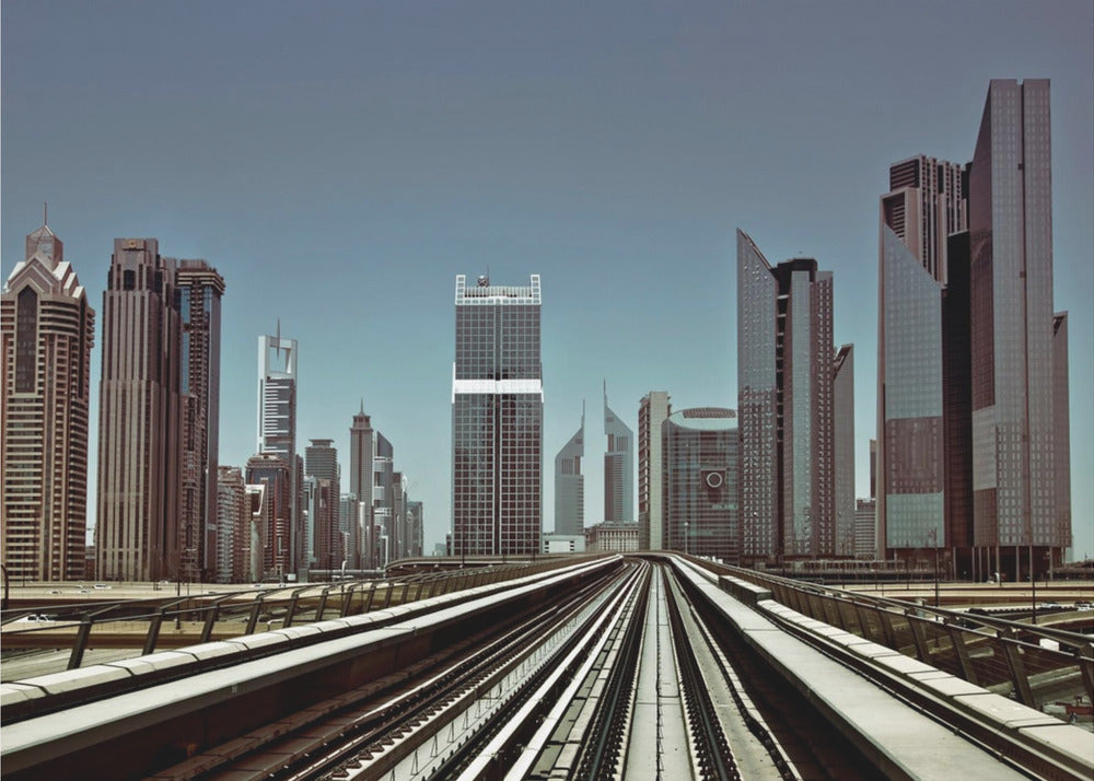 A view from an elevated train track looking down the rails towards the towering skyscrapers of a modern city skyline, under a clear, muted blue sky. Wall Art