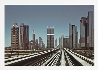 A view from an elevated train track looking down the rails towards the towering skyscrapers of a modern city skyline, under a clear, muted blue sky. Wall Art