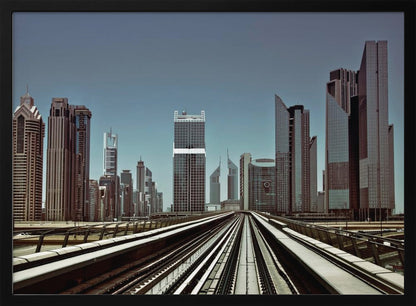 A view from an elevated train track looking down the rails towards the towering skyscrapers of a modern city skyline, under a clear, muted blue sky. Wall Art