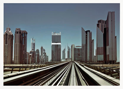 A view from an elevated train track looking down the rails towards the towering skyscrapers of a modern city skyline, under a clear, muted blue sky. Wall Art