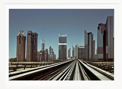 A view from an elevated train track looking down the rails towards the towering skyscrapers of a modern city skyline, under a clear, muted blue sky. Wall Art