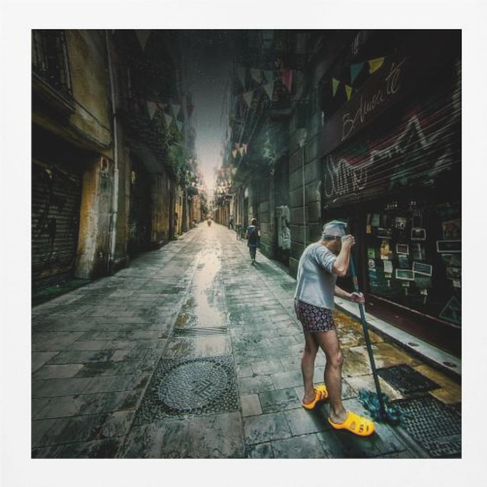 A wide-angle, atmospheric photograph of a man in bright yellow clogs mopping a wet, narrow cobblestone alley. The dark, gritty city street is lined with old buildings and closed storefronts, with another person walking in the distant light at the end of the alley. Wall Art