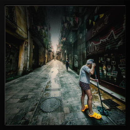 A wide-angle, atmospheric photograph of a man in bright yellow clogs mopping a wet, narrow cobblestone alley. The dark, gritty city street is lined with old buildings and closed storefronts, with another person walking in the distant light at the end of the alley. Wall Art