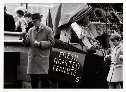 A vintage black and white photograph of an elderly man in a fedora and overcoat feeding a pigeon from his hand at an outdoor market. A sign for 'FRESH ROASTED PEANUTS' is visible next to him, and a young boy in a coat watches nearby. Wall Art