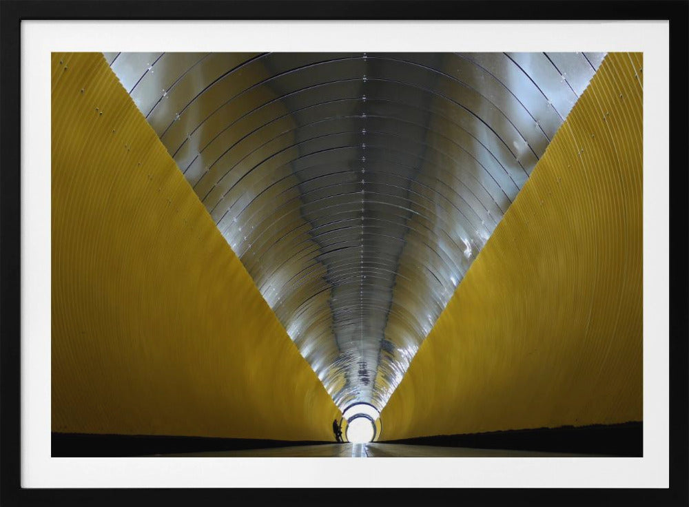A symmetrical, perspective view down a modern, circular tunnel. The lower walls are bright yellow, creating two diagonal lines that converge towards a bright, white light at the far end. The arched ceiling is made of reflective silver metal panels, and a small silhouette stands near the exit. Artwork