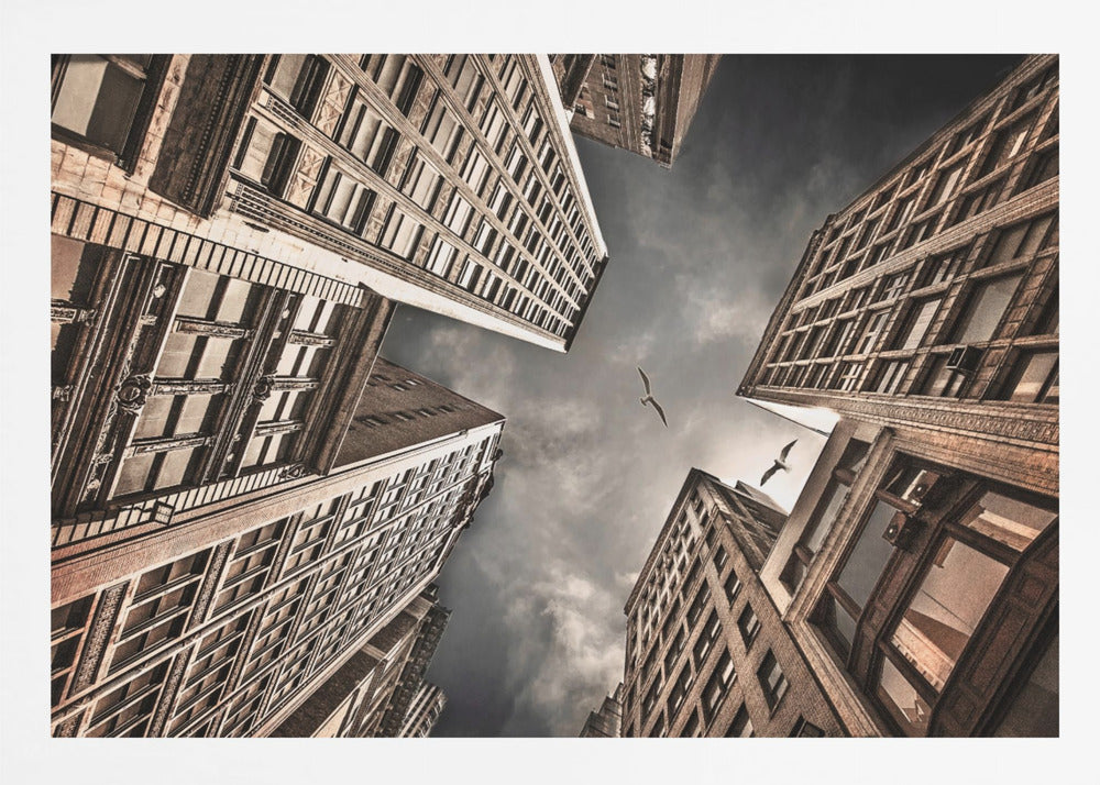 A dramatic, low-angle photograph looking up at the sky between several tall, sepia-toned skyscrapers that converge towards the center. Two birds are seen flying in the moody, dark grey sky. The image has a vintage feel and is presented in a silver frame. Wall Art