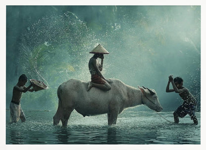 A serene photograph of three young boys playing in a river with a large water buffalo, one boy sits atop the animal while the others splash water, all set against a misty green backdrop and framed in silver. Print