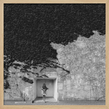 A framed, square black and white photograph showing a stark contrast on an ivy-covered wall. The top half is dense with dark leaves, while the bottom half is a lighter, textured wall. A young girl with long hair, seen from behind, stands in a recessed white doorway in the center. Wall Art