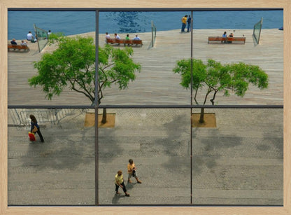 A framed, multi-pane window view showing a composite urban scene. The top panes reflect a sunny day on a wooden boardwalk by blue water, with people relaxing and green trees. The bottom panes show a direct view of a paved street below, with a few pedestrians walking. The window mullions create a grid that divides the distinct scenes. Wall Art