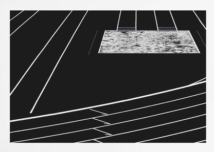 A high-contrast, black and white abstract artwork depicting a running track from an elevated perspective. Stark white lines representing lanes curve across a solid black background. In the upper portion, a rectangular shape filled with a textured, water-like pattern replaces a typical sand pit. The entire piece is presented within a silver frame. Print