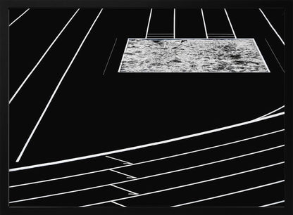 A high-contrast, black and white abstract artwork depicting a running track from an elevated perspective. Stark white lines representing lanes curve across a solid black background. In the upper portion, a rectangular shape filled with a textured, water-like pattern replaces a typical sand pit. The entire piece is presented within a silver frame. Print