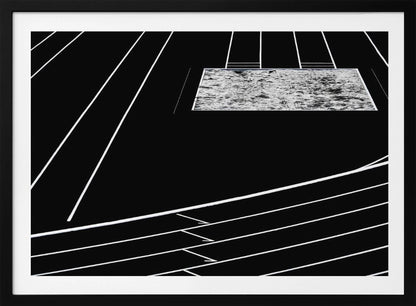 A high-contrast, black and white abstract artwork depicting a running track from an elevated perspective. Stark white lines representing lanes curve across a solid black background. In the upper portion, a rectangular shape filled with a textured, water-like pattern replaces a typical sand pit. The entire piece is presented within a silver frame. Print
