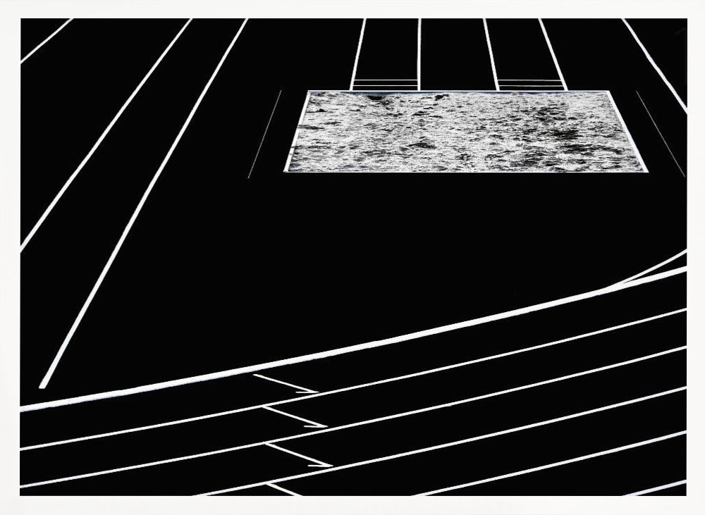 A high-contrast, black and white abstract artwork depicting a running track from an elevated perspective. Stark white lines representing lanes curve across a solid black background. In the upper portion, a rectangular shape filled with a textured, water-like pattern replaces a typical sand pit. The entire piece is presented within a silver frame. Print