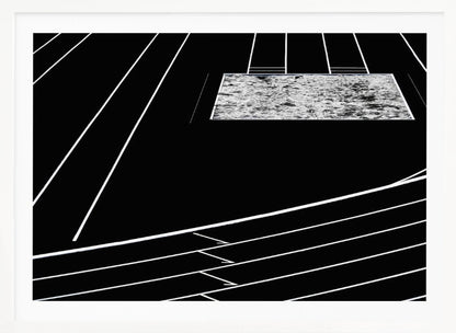 A high-contrast, black and white abstract artwork depicting a running track from an elevated perspective. Stark white lines representing lanes curve across a solid black background. In the upper portion, a rectangular shape filled with a textured, water-like pattern replaces a typical sand pit. The entire piece is presented within a silver frame. Print