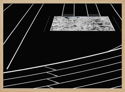 A high-contrast, black and white abstract artwork depicting a running track from an elevated perspective. Stark white lines representing lanes curve across a solid black background. In the upper portion, a rectangular shape filled with a textured, water-like pattern replaces a typical sand pit. The entire piece is presented within a silver frame. Print