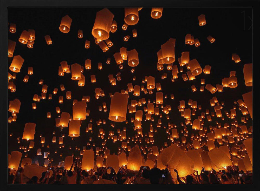 A framed photograph of a sky lantern festival at night, with hundreds of warm, orange-glowing lanterns floating up into the pitch-black sky from a crowd of people below. Artwork