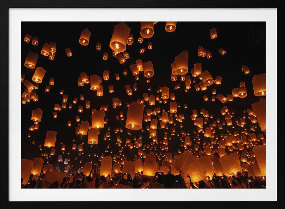 A framed photograph of a sky lantern festival at night, with hundreds of warm, orange-glowing lanterns floating up into the pitch-black sky from a crowd of people below. Artwork