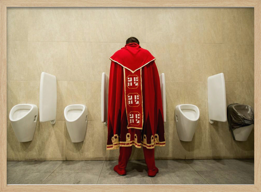 A back view of a person wearing an elaborate, long red and gold cape, standing at a urinal in a modern public restroom with beige tiled walls and multiple white urinals. Artwork