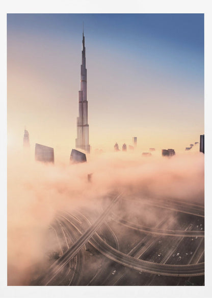 An aerial photograph of the Burj Khalifa in Dubai, towering over a thick blanket of pink and orange-hued fog at sunrise. Below the fog, a complex highway interchange is visible, with the clear blue sky above. Wall Art
