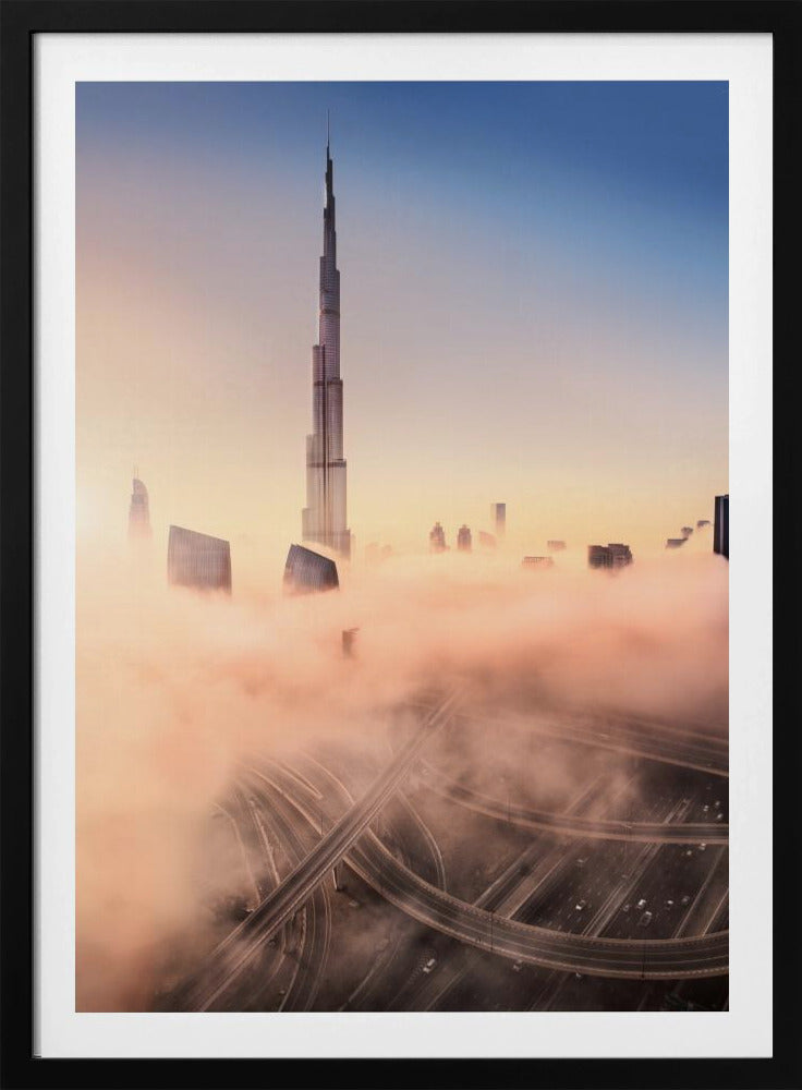 An aerial photograph of the Burj Khalifa in Dubai, towering over a thick blanket of pink and orange-hued fog at sunrise. Below the fog, a complex highway interchange is visible, with the clear blue sky above. Wall Art