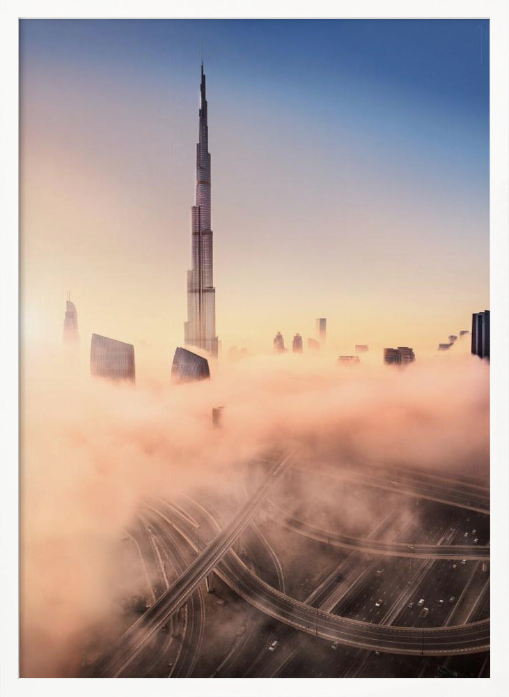 An aerial photograph of the Burj Khalifa in Dubai, towering over a thick blanket of pink and orange-hued fog at sunrise. Below the fog, a complex highway interchange is visible, with the clear blue sky above. Wall Art