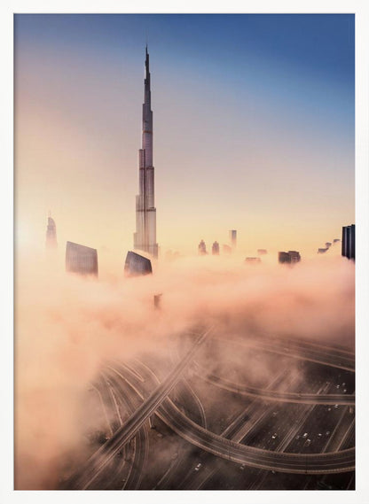 An aerial photograph of the Burj Khalifa in Dubai, towering over a thick blanket of pink and orange-hued fog at sunrise. Below the fog, a complex highway interchange is visible, with the clear blue sky above. Wall Art