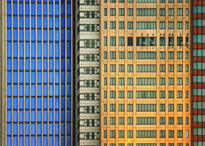 An abstract architectural photograph showing the colorful gridded facades of three adjacent skyscrapers, featuring a blue-windowed building, a white building, and a yellow building, all contained within a silver frame. Wall Art