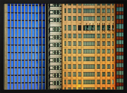 An abstract architectural photograph showing the colorful gridded facades of three adjacent skyscrapers, featuring a blue-windowed building, a white building, and a yellow building, all contained within a silver frame. Wall Art