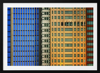 An abstract architectural photograph showing the colorful gridded facades of three adjacent skyscrapers, featuring a blue-windowed building, a white building, and a yellow building, all contained within a silver frame. Wall Art