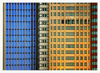 An abstract architectural photograph showing the colorful gridded facades of three adjacent skyscrapers, featuring a blue-windowed building, a white building, and a yellow building, all contained within a silver frame. Wall Art