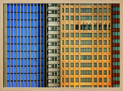 An abstract architectural photograph showing the colorful gridded facades of three adjacent skyscrapers, featuring a blue-windowed building, a white building, and a yellow building, all contained within a silver frame. Wall Art