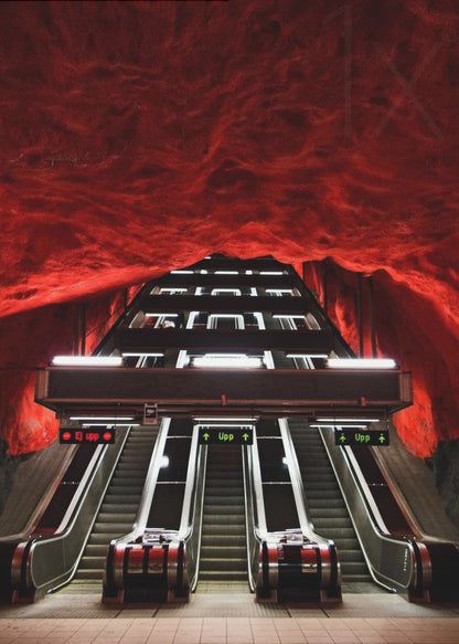 A dramatic low-angle shot looking up a series of escalators in a subway station with a cavernous, rough-textured ceiling glowing an intense, fiery red. Decor