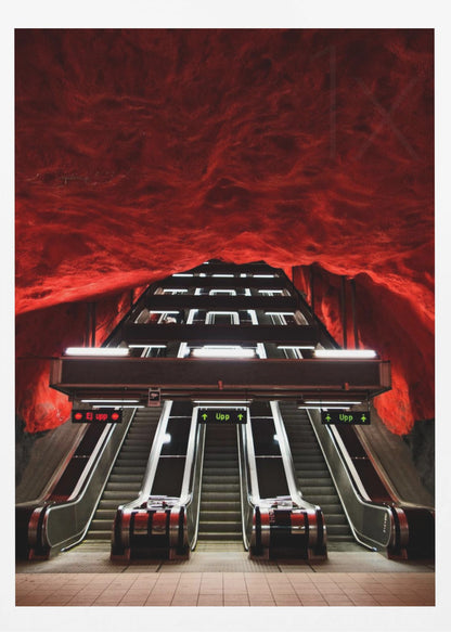A dramatic low-angle shot looking up a series of escalators in a subway station with a cavernous, rough-textured ceiling glowing an intense, fiery red. Decor